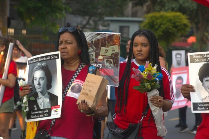 Manifestantes exibem cartazes com imagens de Ana Rosa Kucinski e Sonia Maria Moraes Angel, assassinadas pela Ditadura Militar