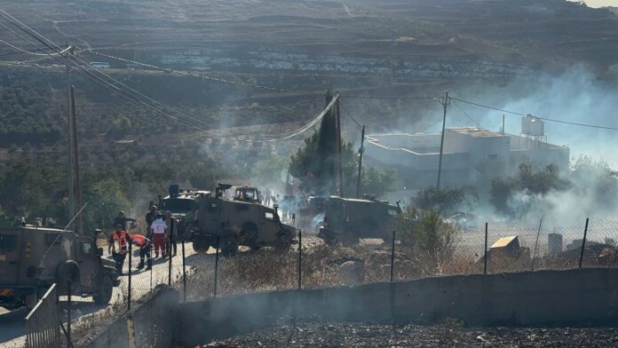 Jipes militares de Israel circulam pela estrada na vila palestina de Sarra, perto de Nablus, enquanto a defesa civil e moradores combatem as chamas de uma casa atacada por colonos israelenses (foto: Muhammad Ateeq/Middle East Eye)